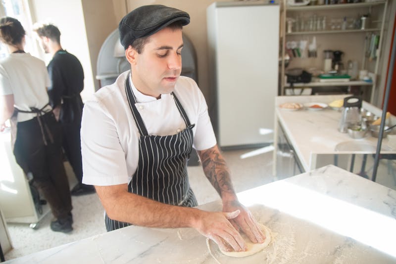 Chef hand-stretching pizza dough in the kitchen